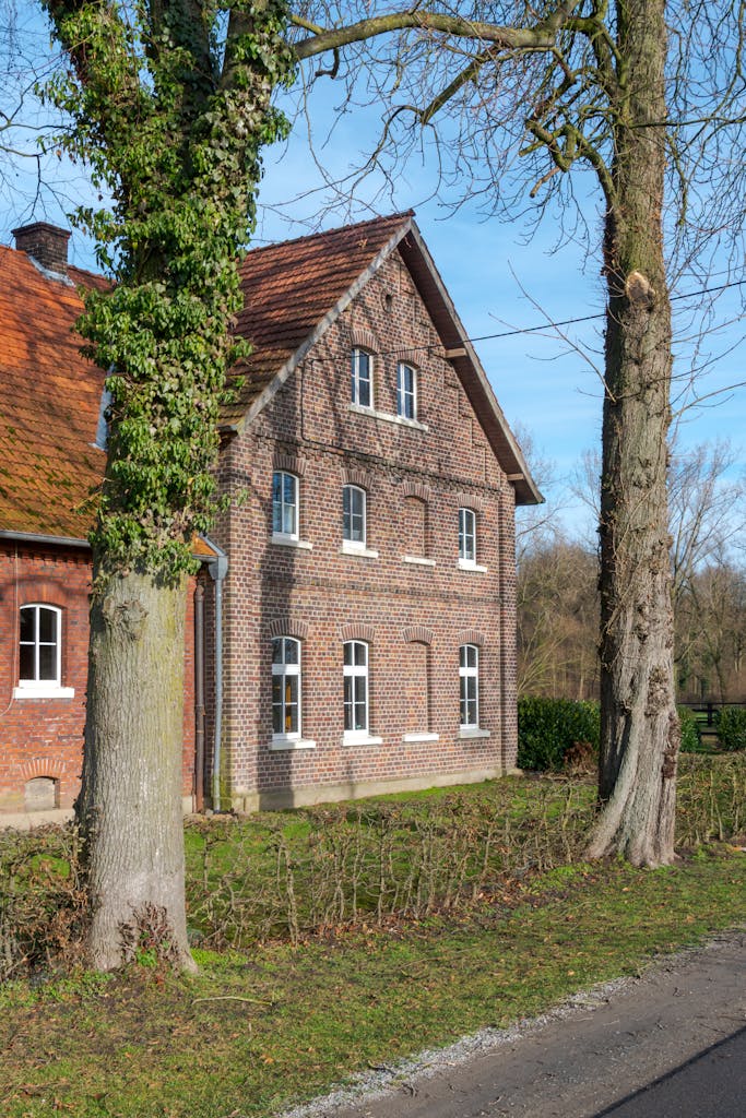 Brick house with red-tiled roof in Coesfeld on a sunny day, surrounded by trees.